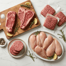 The Dude Food Dude Meat Box by Dude Food is displayed on a countertop, featuring Kansas City Strip Steaks, American Ground Beef, burger patties, and Boneless Skinless Chicken Breasts arranged with herbs, lemon slices, salt, and pepper.