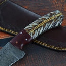 A close-up of the Texan Knives 8.5" Damascus Steel Blade hunting knife with a pine cone resin handle, resting on its leather sheath—an excellent pick among the Best Knives for Hunting.
