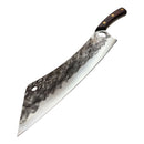 The Spaceman Knives Meteor Series Mega Chef, with a hammered steel blade and wooden handle, lies on marble next to black fabric and a textured black Spaceman Knives box.