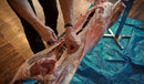 A man cutting a piece of meat on a table using the SpitJack 7" Stainless Steel Meat Trussing Needle and Butcher's Cooking Twine Bundle.