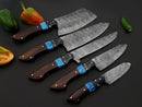 Five Texan Knives Best Chef Knives Sets—13" handmade Damascus steel kitchen knives with wenge resin handles and leather sheaths—are arranged on a black surface with green and orange peppers for a premium chef knife set.