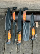 The Texan Knives Damascus Steel Handmade Chef Knife Set with Sharpener features dark hammered blades and wood handles with orange resin. Arranged on rustic wood beside a brown knife roll, it's the perfect gift for a wife, husband, or Valentine’s Day.