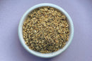 A white bowl filled with World Spice Elderflower by World Spice rests on a light purple surface, perfect for crafting soothing elderflower tea or delicate infusions.