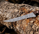 The Texan Knives Fishing Fillet & Boning Knife—13" Damascus steel with a camel bone and rosewood handle—rests on a textured tree trunk, its blade showing the signature wavy patterns, and comes with a leather sheath.