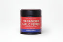 A jar of World Spice Habanero Garlic Pepper, bearing a distinctive red and blue label, rests against a simple white background. This handcrafted blend combines the bold heat of habanero, aromatic garlic, and top-quality Vietnamese black pepper for an unforgettable kick.