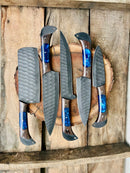The Texan Knives Handmade Damascus Steel Chef Knife Set includes six knives with hammered gray blades, dark wooden handles, and blue resin accents, displayed on a round board—a perfect wedding or Valentine’s Day gift.