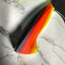A close-up of the Spaceman Knives EM Wave Chef Knife, featuring a vibrant Damascus steel blade with red, orange, yellow, and black diagonal stripes, rests on white marble—an ideal choice for any professional kitchen.