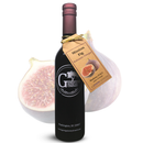 A dark glass bottle of Georgetown Olive Oil Co. Mission Fig Balsamic Vinegar, featuring a fig illustration on the label, is displayed in front of a large, halved mission fig in the background. A tan tag tied to the bottle showcases a fig image and product details, emphasizing its rich balsamic vinegar origins from Modena, Italy.