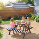 Three children enjoy snacks at the DirectDeals Fir Wood Kids Picnic Table with 2 Built-in Benches and Umbrella in a sunny, flower-filled backyard.