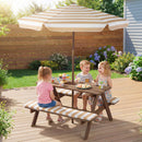 Three children enjoy cupcakes outdoors at the Fir Wood Kids Picnic Table with 2 Built-in Benches and Umbrella by DirectDeals, set in a backyard with a wooden fence, flowers, and deck.