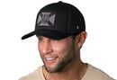 A man with light eyes and a short beard smiles while wearing the Haka Hat Florida Flag Trucker Hat, a black tactical snapback by Haka Hat, paired with a beige shirt against a white background.