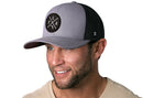 Bearded man wearing the Haka Hat Florida Trucker Hat | Gray-Black FLA X Snapback, featuring a circular black and white FLA X patch. He pairs the stylish snapback with a beige shirt.