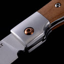 Close-up of the Messermeister Folding Steak Knife - 4", featuring a metal blade, silver bolster with copper screw, and wooden handle, displayed against a black background.
