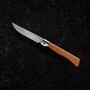 The Messermeister Folding Steak Knife - 4" features a shiny steel blade and wooden handle, shown open on a dark, textured surface.