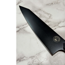A sleek black Dark Matter Kiritsuke by Spaceman Knives, made from premium 7CR17MOV-X steel, rests on white marble, its signature logo gleaming on the blade.