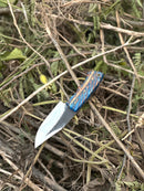 The Texan Knives Good Hunting Knives features a 9" handmade J2 steel blade and a colorful epoxy resin handle, shown outdoors on dry twigs and green leaves. Includes leather sheath.