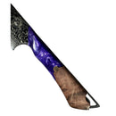 A close-up of the Spaceman Knives Gravity Series Nakiri handle shows polished wood, vibrant purple resin, and intricate metalwork. The blade’s partially visible edge reveals a striking Damascus pattern.