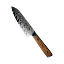 The Spaceman Knives Interstellar Petty Chef Knife by Spaceman Knives, featuring a patterned Damascus steel blade and wooden handle, rests on a light-colored marble surface.