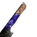 A close-up of the Spaceman Knives Gravity Series Utility Knife handle showcases swirling purple resin, natural wood grain, and a metallic accent, with part of the Damascus steel blade visible against a white background.