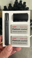 A hand holds The Immaculate Beard Safety Razor set, featuring a textured black metal handle, a matching razor head, and two packs of double edge platinum coated safety razor blades. Several blurred black-capped bottles appear in the background.