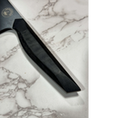 Close-up of the Spaceman Knives Dark Matter Kiritsuke handle on white marble, showcasing its textured grip and a glimpse of the 7CR17MOV-X steel blade.