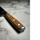 A close-up of the Spaceman Knives Interstellar Petty Chef Knife by Spaceman Knives, featuring a wooden handle with metal rivets and a gold emblem, resting on a light marbled surface.