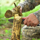 A person in camouflage uses the Texan Knives Custom Handmade 9" Damascus Steel Hunting Knife with G10 Handle & Leather Sheath to whittle a thick stick outdoors on green grass.