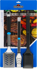 Three barbecue tools—a spatula, tongs, and a Palmyra bristle grill brush—from the Napoleon 3-Piece Starter Tool Set Essential Series hang in front of grilled food, shown in blue Napoleon Grills packaging.