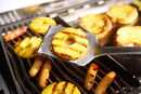 Grilled pineapple rings and sausages cook on a barbecue as a Napoleon Grills Premium Grill Spatula PRO Series (GATL007) lifts a pineapple ring to reveal perfect grill marks.