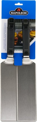 The Napoleon Griddle Spatula 2-Piece Set for Griddles (GATL011) by Napoleon Grills includes two stainless steel spatulas with black handles, packaged on a blue branded card featuring burgers grilling in the background.