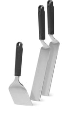 Three stainless steel spatulas from the Napoleon Griddle Starter 3-Piece Set (GATL012) by Napoleon Grills stand upright on their blades, black handles up, each varying in shape and length—perfect for any griddle setup.