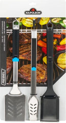 The Napoleon Grills Essential Series Silicone Basting Brush (GATL005) is shown in packaging, with heat-resistant bristles, displayed in front of grilled meats and vegetables.