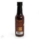 A dark glass bottle of Powerful Pepper Company Chipotle Ghost & Black Garlic Hot Sauce stands upright. The label features a description, QR code, barcode, and website URL, with gold text and graphics on a brown background.