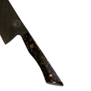 The Spaceman Knives Galaxy Series Nakiri Knife, featuring a black and gold-speckled handle, is set diagonally against a swirling galaxy backdrop—blending cosmic flair with precision for vegetable prep.