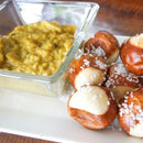 A glass dish of Terrapin Ridge Farms Garlic Kraut Mustard - Quart sits next to salted soft pretzel bites on a white plate atop a wooden surface—a flavorful deli-style mustard perfect for snacking or as a sandwich condiment.