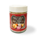 A 4oz glass jar of SALTOPIA Infused Sea Salts, with a red label featuring garlic and onions and a white lid, is included in the Saltopia Garlic Lovers Gift Set—an ideal gift for garlic enthusiasts.