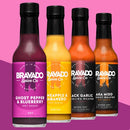 Four Bravado Spice Co. hot sauces—Ghost Pepper & Blueberry, Pineapple Habanero, Black Garlic Carolina Reaper, and Aka Miso—are showcased against a pink background, featuring their fan-favorite Bravado Spice Co Ghost Pepper & Blueberry Hot Sauce, as seen on Hot Ones Season 3.