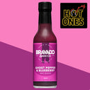 A bottle of Bravado Spice Co Ghost Pepper & Blueberry Hot Sauce by Bravado Spice Co is showcased against a pink background, with the Hot Ones logo in the top right corner—an iconic selection from Hot Ones Season 3 for fans of bold ghost pepper flavors.