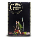 A box labeled Georgetown Olive Oil Co. is displayed on a wooden surface against a dark background, featuring the Georgetown Olive Oil Co 3 Bottle Extra Virgin Olive Oil Gift Set with three green bottles of premium extra virgin olive oil, accompanied by herbs and spices.