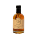 A glass bottle from Under The Bark Syrup Co, filled with amber ginger maple syrup and labeled "Under The Bark Syrup Co Ginger Maple Syrup," features a maple leaf illustration and has a black cap.