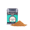 A Spicewalla Gingerbread Spice tin from Spicewalla stands upright beside a small mound of brown gingerbread spice powder on a white surface, ideal for bringing warm, festive flavor to classic gingerbread cookies and holiday baking.