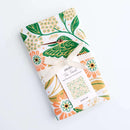 The Gingiber Hummingbird Tea Towel by Gingiber features a vibrant floral design in green, orange, and yellow on soft flour sack cotton, tied with a cream ribbon—ideal as a decorative touch for your kitchen.