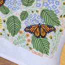 The Gingiber Monarch Garden Tea Towel features a vibrant monarch butterfly among green leaves and colorful flowers, printed on soft flour sack cotton with “GINGIBER” below, making it a decorative kitchen accent.