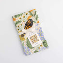 The Gingiber Monarch Garden Tea Towel, made from flour sack cotton, features a vibrant floral and butterfly design. It’s folded with a cream ribbon and “Tea Towel” tag, displayed on a white background.
