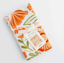 The Gingiber Poppy Tea Towel by Gingiber, featuring orange and green floral designs, is folded and tied with a cream ribbon and matching tag on a white background—ideal as a decorative kitchen accent.