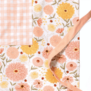 The Gingiber Zinnia Apron by Gingiber features floral-patterned cotton in peach, yellow, and cream with a pink gingham pocket and adjustable peach strap—making it a stylish addition to any kitchen.