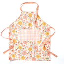 The Gingiber Zinnia Apron by Gingiber is a floral cotton cooking apron with yellow, orange, and pink flowers, a large pink and white gingham pocket, and peach neck and waist ties, shown laid flat on a white background.