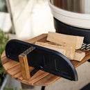 A close-up of stacked firewood on a wooden side table features the Gozney Dome XL Gen 2 Door by Gozney nearby, with a blurred grill or fire pit in the background—perfect for smoking and slow-roasting.