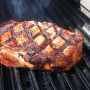 A thick, grilled steak with steakhouse-style sear marks and a crispy, browned crust sits on a hot pellet grill, enhanced by the Smokin Brothers GrillGrate Searing Set from Smokin Brothers, with smoke rising around it.