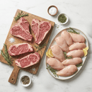 The Dude Food Guys Meat Box by Dude Food features raw beef steaks, including premium Kansas City Strip Steaks, and boneless chicken breasts artfully arranged on a wooden board and a white plate, garnished with fresh herbs and lemon slices. Small bowls of salt, pepper, and rosemary surround the display on a marble surface—perfect for preparing savory game day snacks.